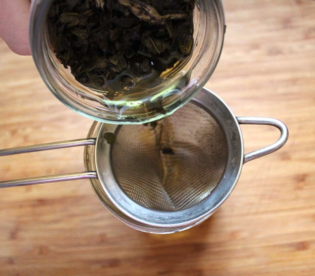 Filtering echinacea tincture through a fine mesh strainer.