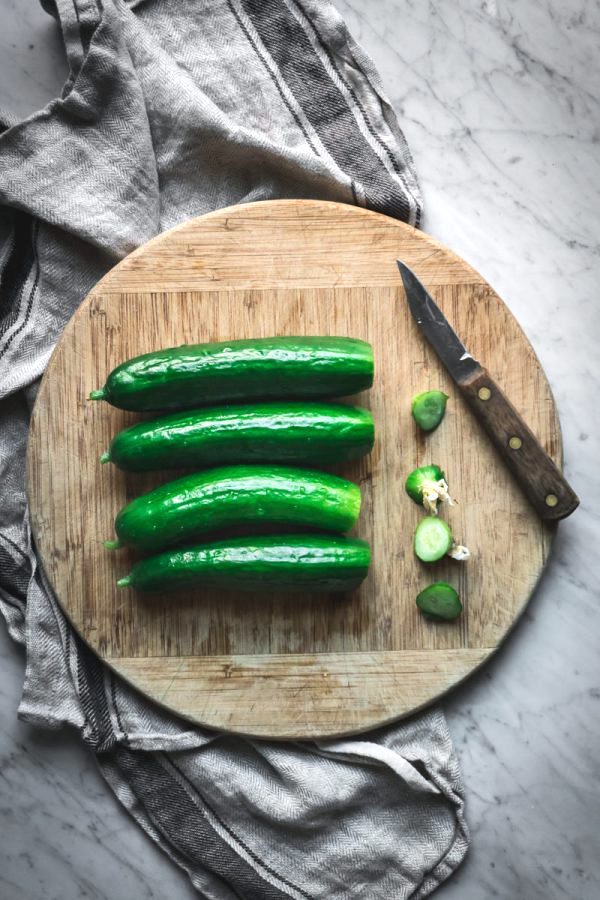Preparing cucumbers for fermented pickles ~ Four cucumbers on a cutting board with blossom end removed.