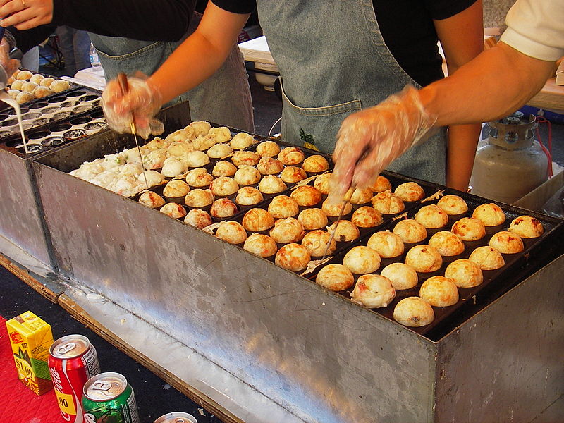 A street vendor preparing Takoyaki in a commercial pan.