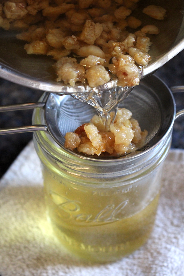 Filtering the cracklins from leaf lard using a fine mesh strainer.