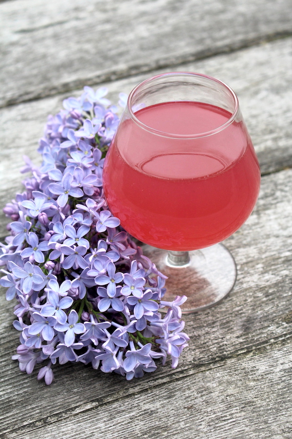 glass of lilac wine on a table with lilac flowers