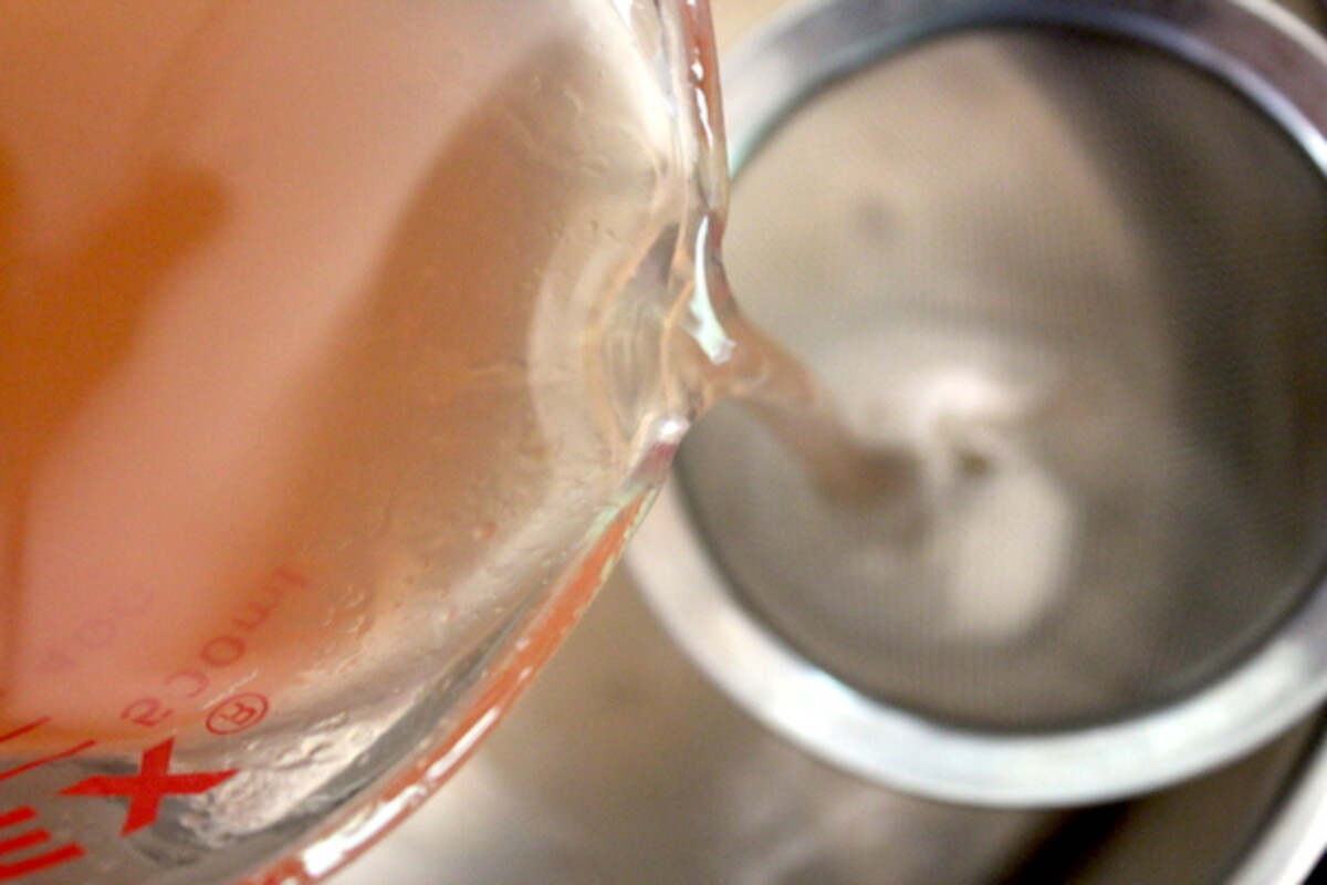 Filtering extracted peach juice through a fine mesh strainer for making peach jelly