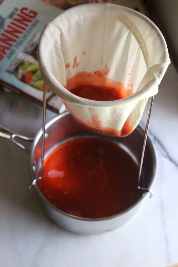 Straining strawberry jelly though a jelly bag positioned over a saucepan