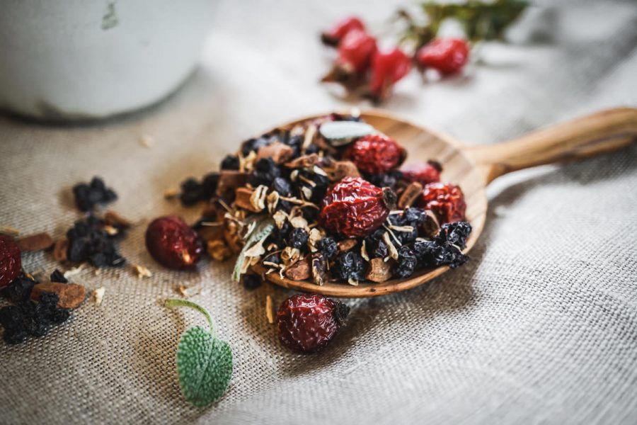 loose leaf tea with rose hips rest in a wooden spoon