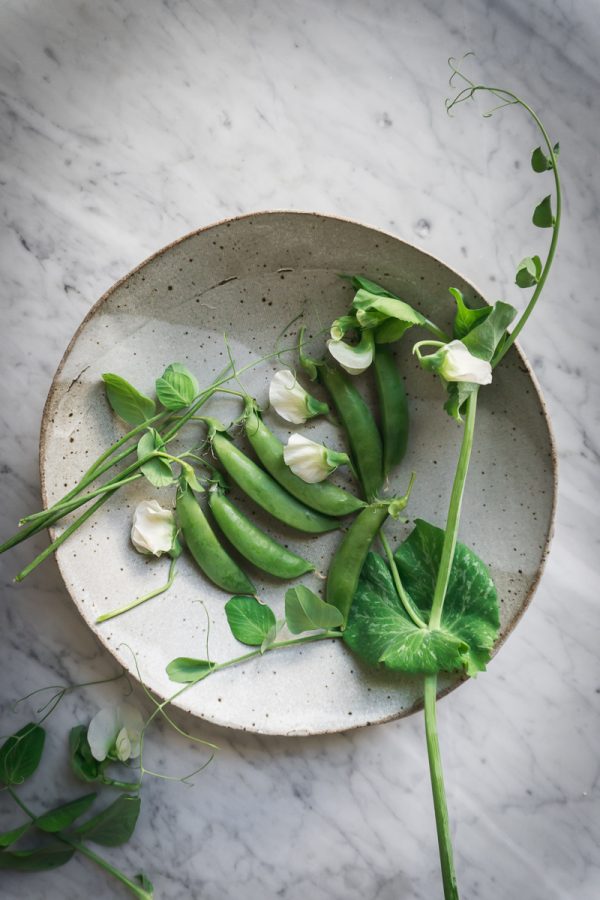 Snap peas and pea flowers in a bowl on marble counter. 