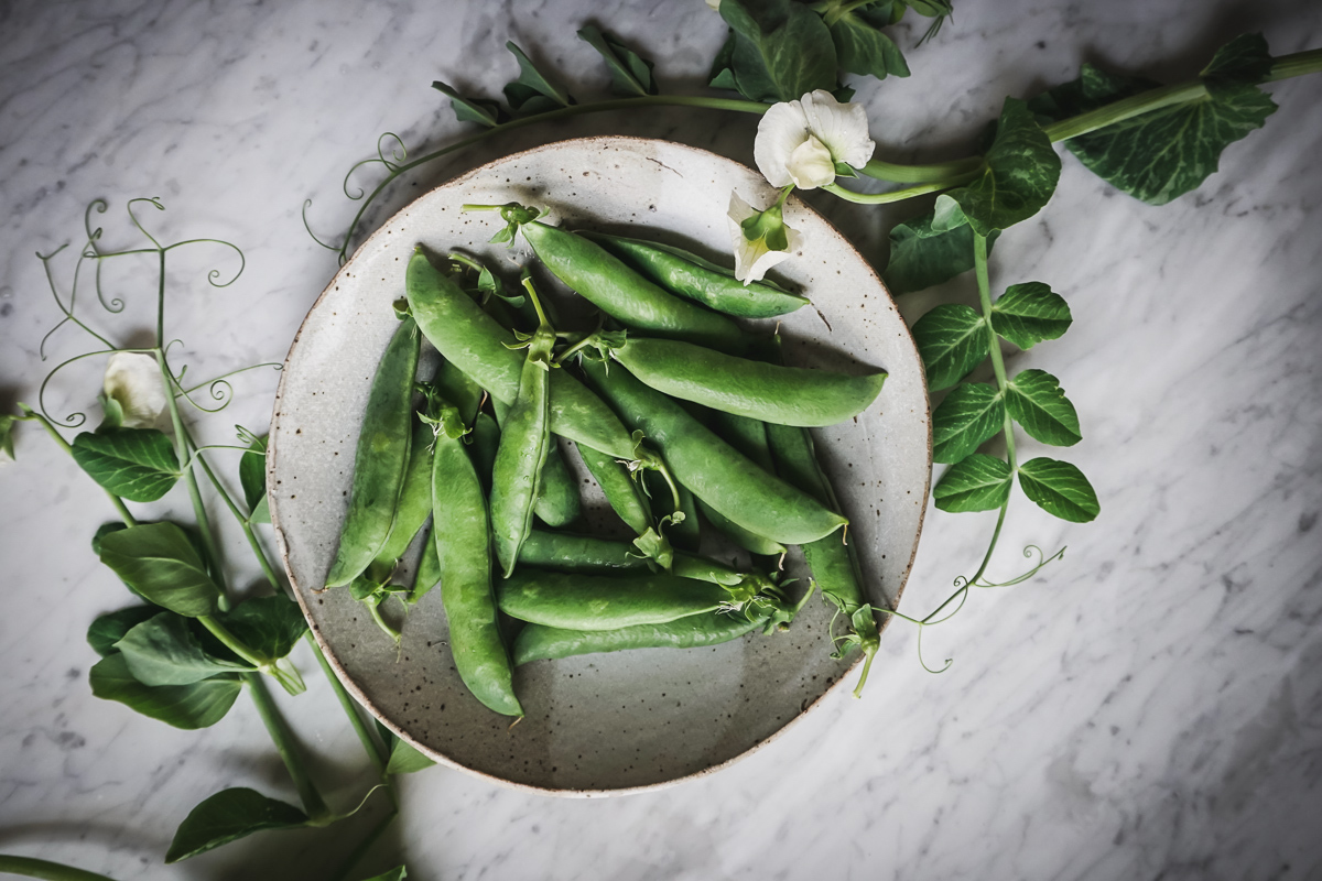 A bowl of fresh, home grown peas with vines and flowers