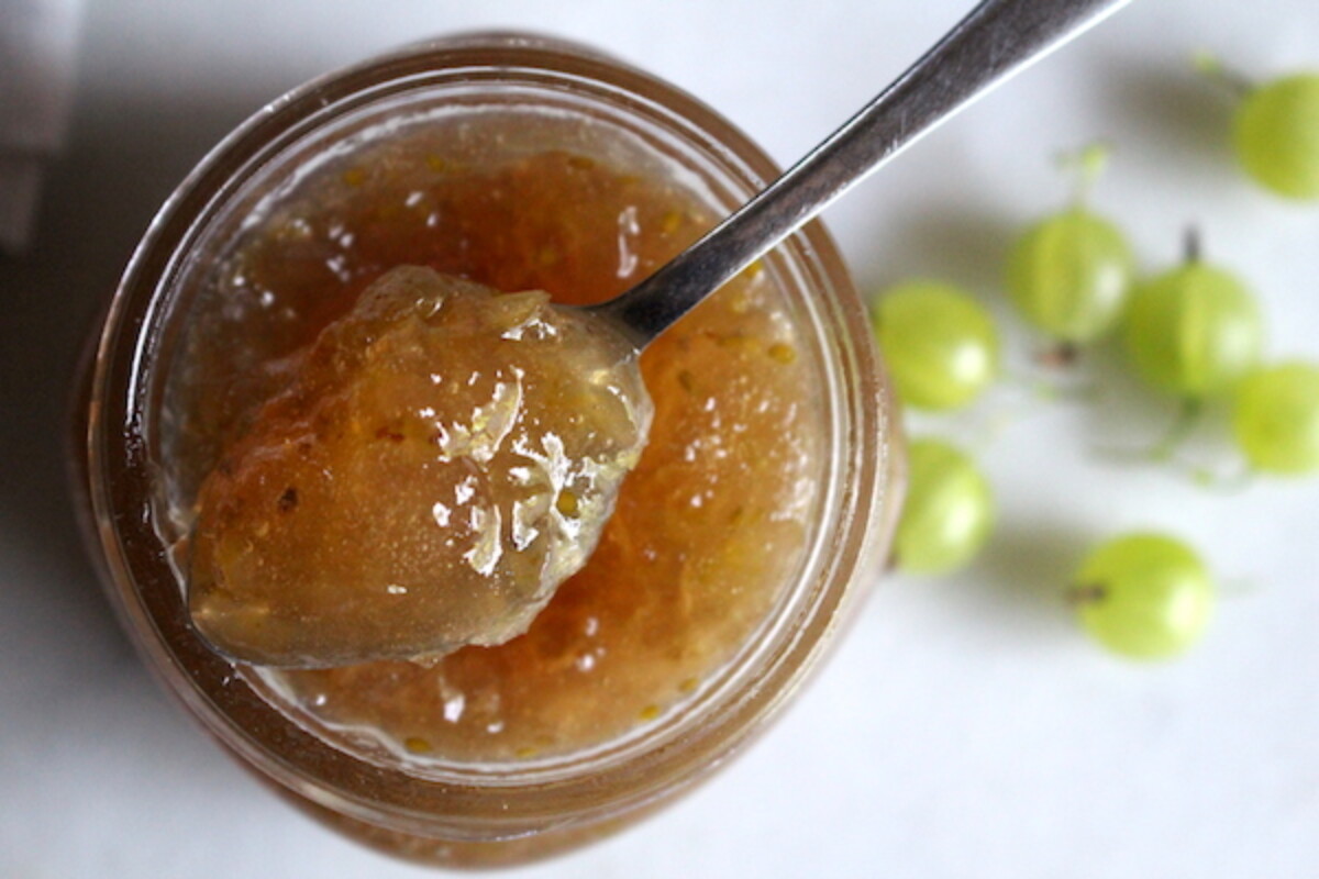 A jar of gooseberry jam, top view with a spoon holding a bit of jam to show the firm set achieved even without pectin.
