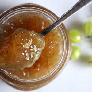 A jar of gooseberry jam, top view with a spoon holding a bit of jam to show the firm set achieved even without pectin.