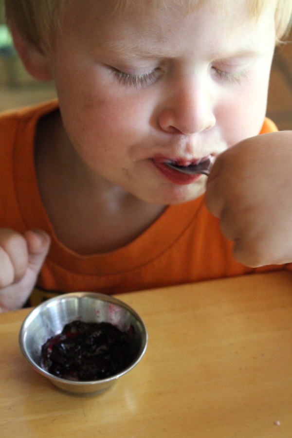 Child eating blackcurrant jelly out of a small bowl
