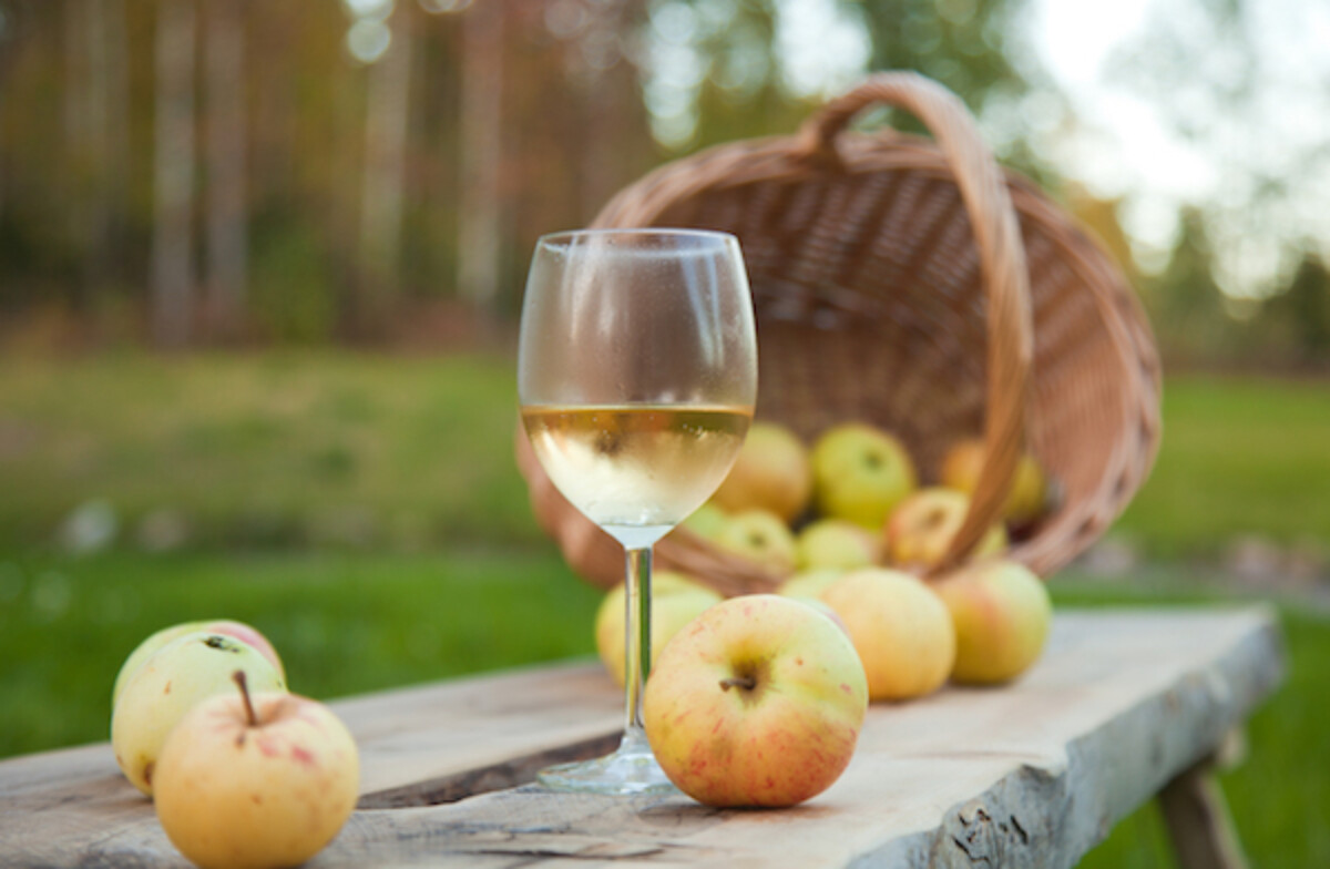 Glass of apple wine on a table in front of a basket of apples