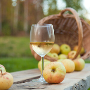 Glass of apple wine on a table in front of a basket of apples