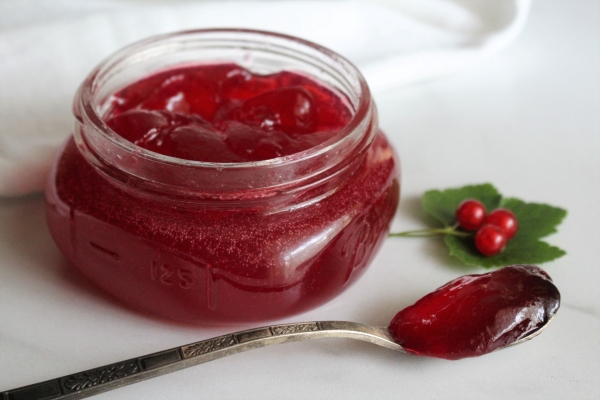 Open jar of homemade redcurrant jelly, with jelly on a spoon next to it