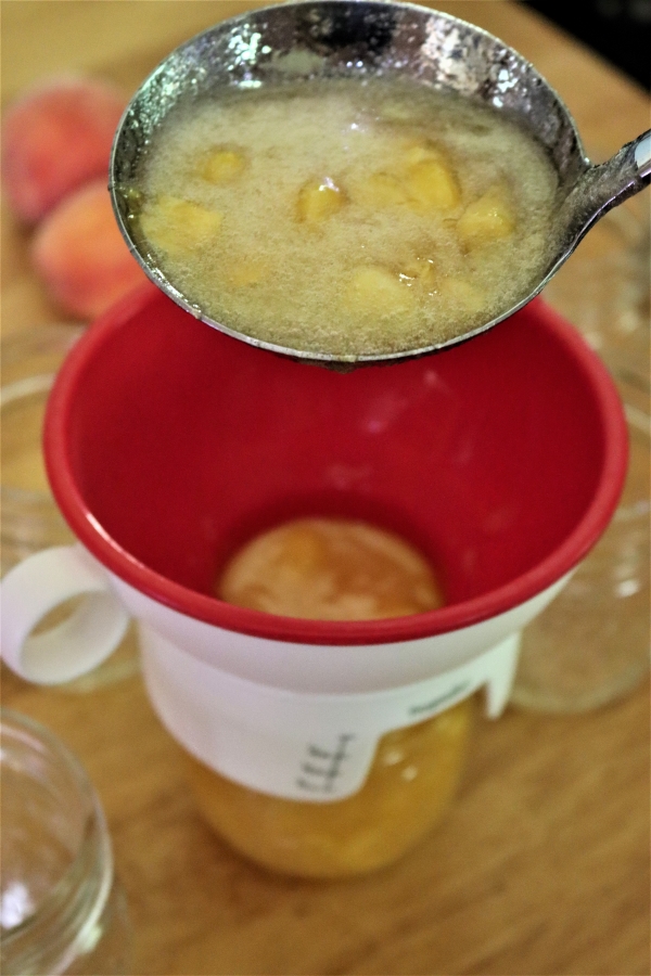 Ladling peach jam into canning jars.