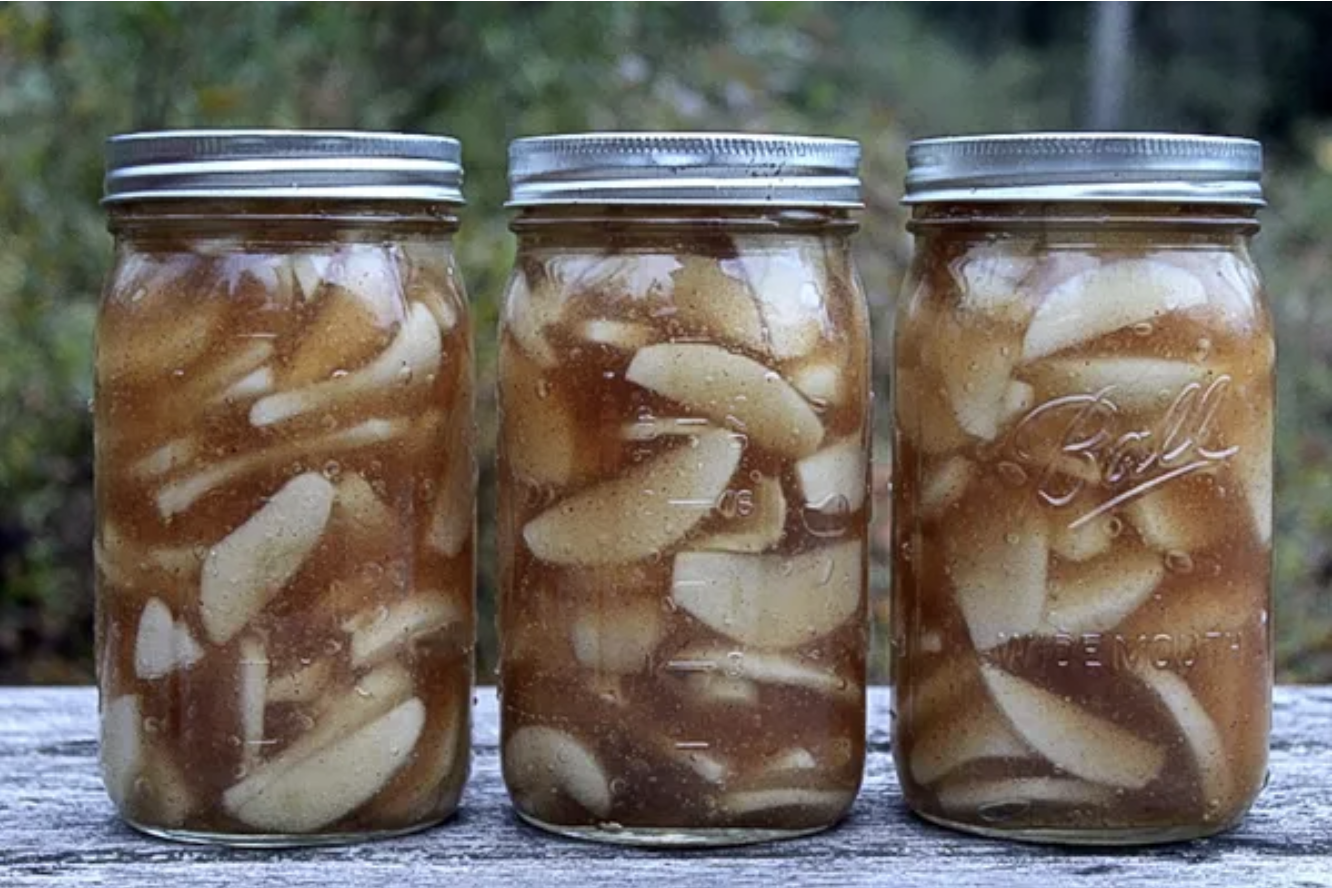Three quart ball mason jars of home canned apple pie filling on a wood table.