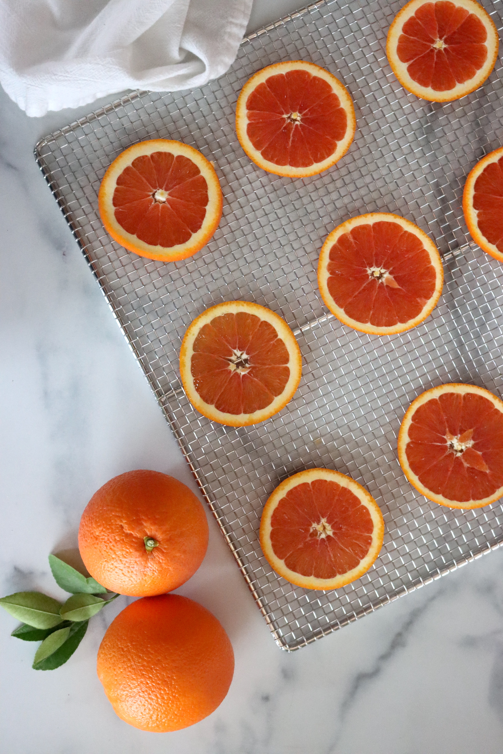 Dried Cara Cara orange slices on a mesh drying rack beside whole oranges and orange leaves