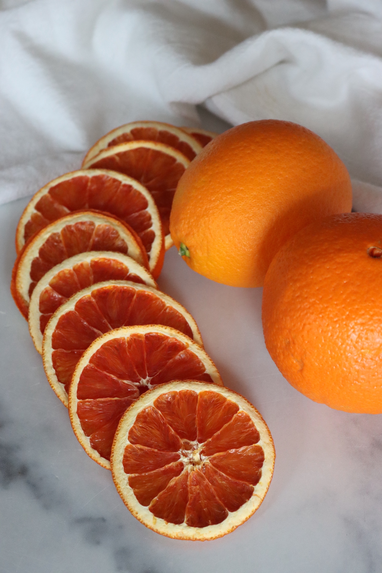 Dried orange slices lined up beside whole oranges on a white towel