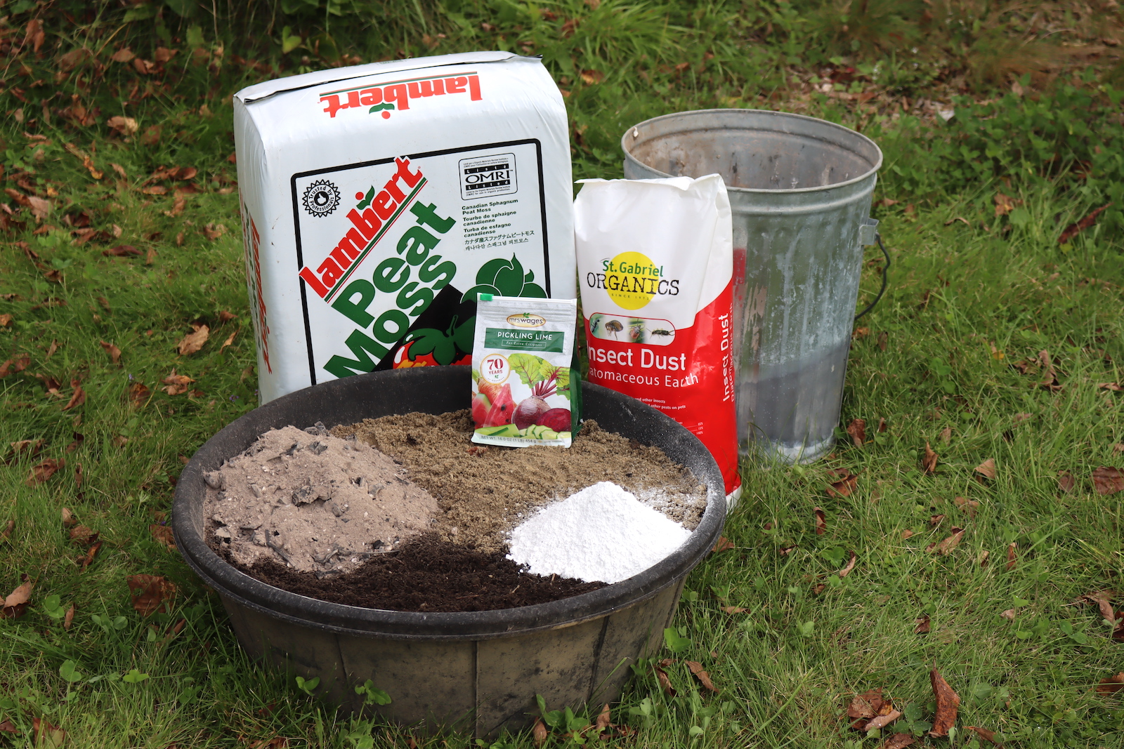 Chicken dust bath ingredients in a rubber pan, with peat moss, diatomaceous earth, pickling lime, and a can of wood ash