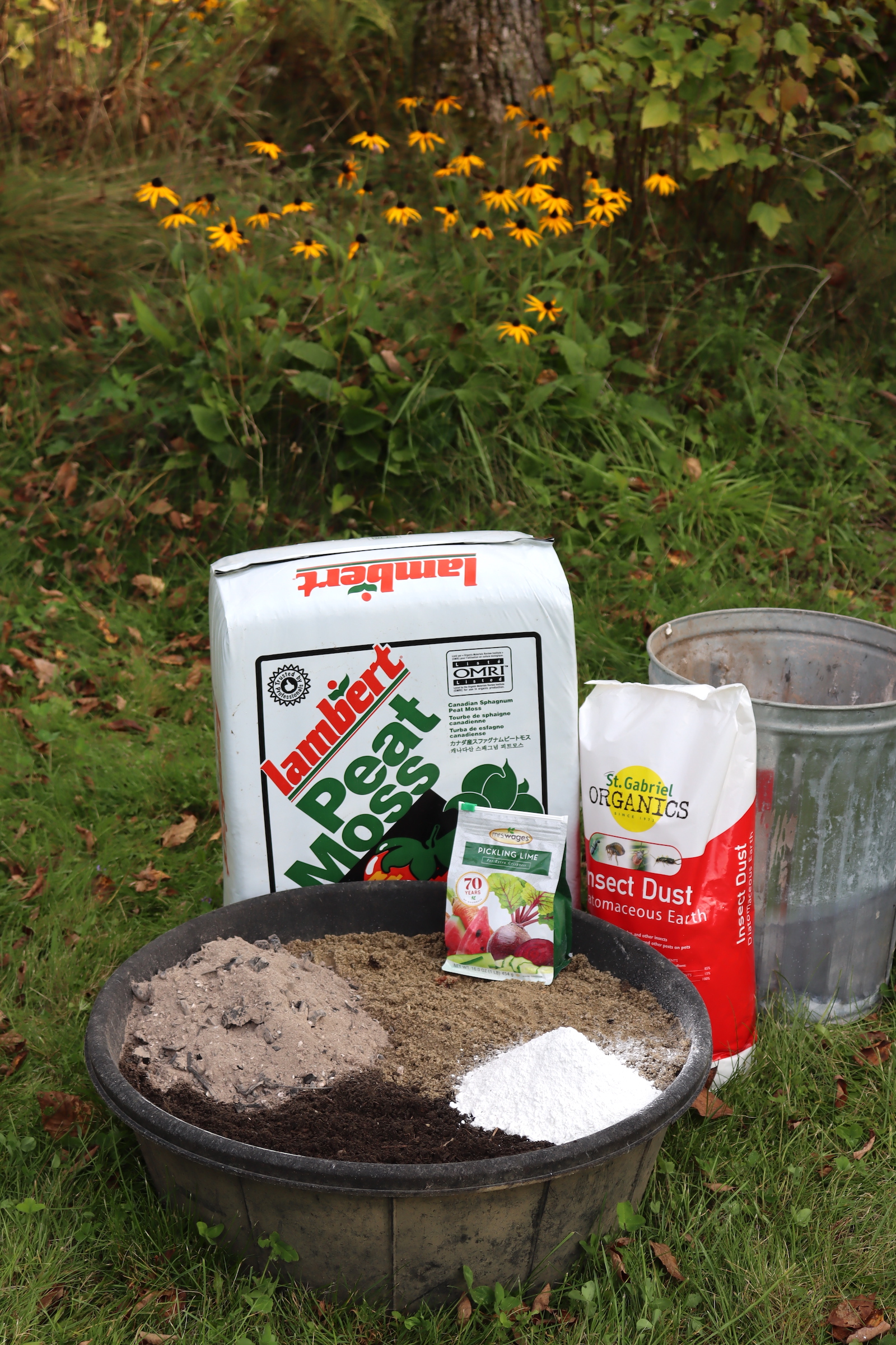 Chicken dust bath ingredients in a rubber pan beside bags of peat moss, diatomaceous earth, and pickling lime